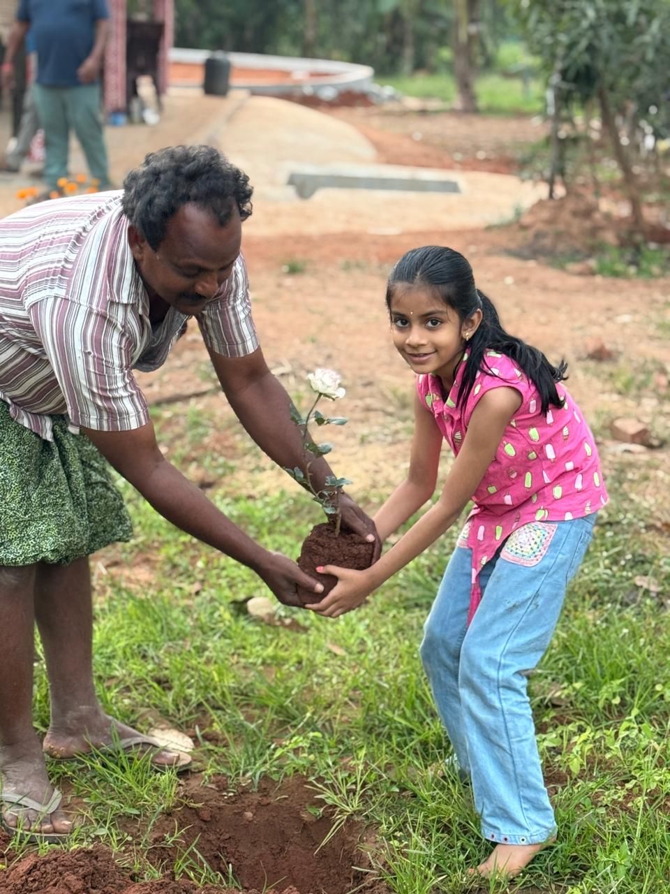 A girl and a man holding a rose plant, ready to plant it