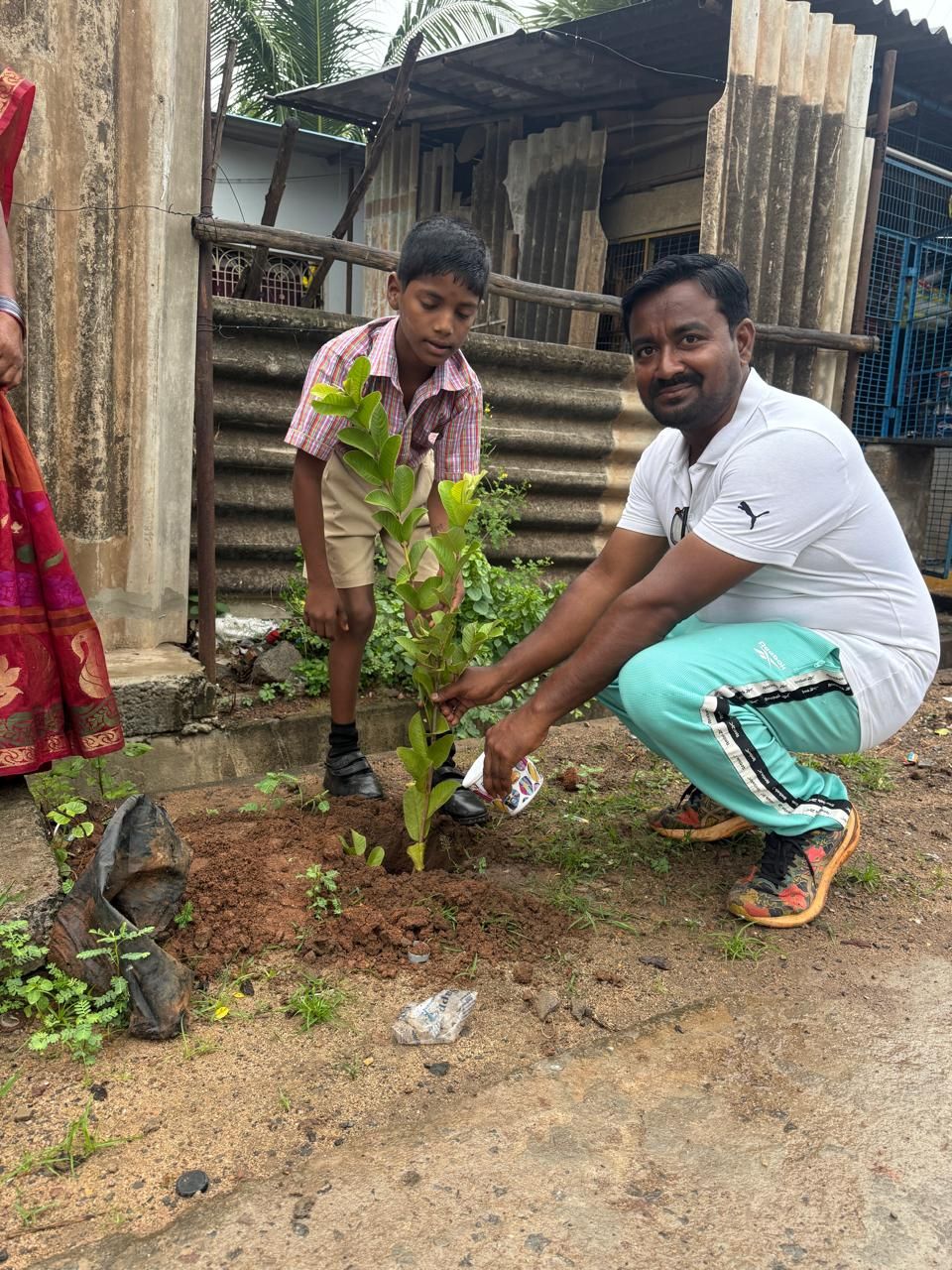 A schoolboy and a volunteer planting and watering a sapling